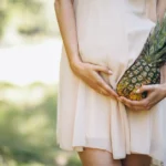 Pregnant woman holding fresh pineapple while touching belly - can pregnant women eat pineapple safely during pregnancy