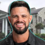 Steven Furtick smiling in front of his luxury Waxhaw mansion showing the stone exterior and landscaped grounds of his North Carolina estate