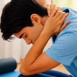 Person experiencing inomyalgia neck pain while sitting on exercise mat with foam roller nearby