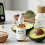 Keto drops bottle with dropper next to fresh avocado halves, MCT oil, pink Himalayan salt, and blood ketone meter showing 1.2 reading on white marble countertop