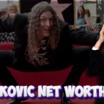 Al Yankovic performing on stage, smiling and holding a microphone during a live concert, reflecting his career and net worth.