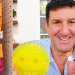 Aaron Krause holding a yellow Scrub Daddy sponge next to store shelf displaying Scrub Daddy and Scrub Mommy products, illustrating scrub daddy net worth success story.