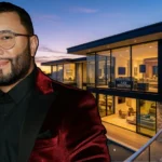 Alex Sensation standing in front of a modern luxury home with floor-to-ceiling glass walls, multi-level design, and city views at sunset